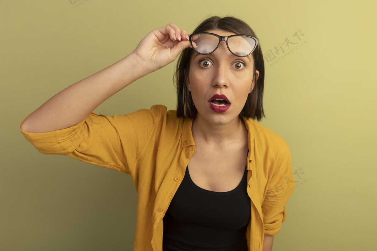 脸震惊的美女拿着眼镜 看着橄榄绿墙上孤立的前方衣服眼镜感觉