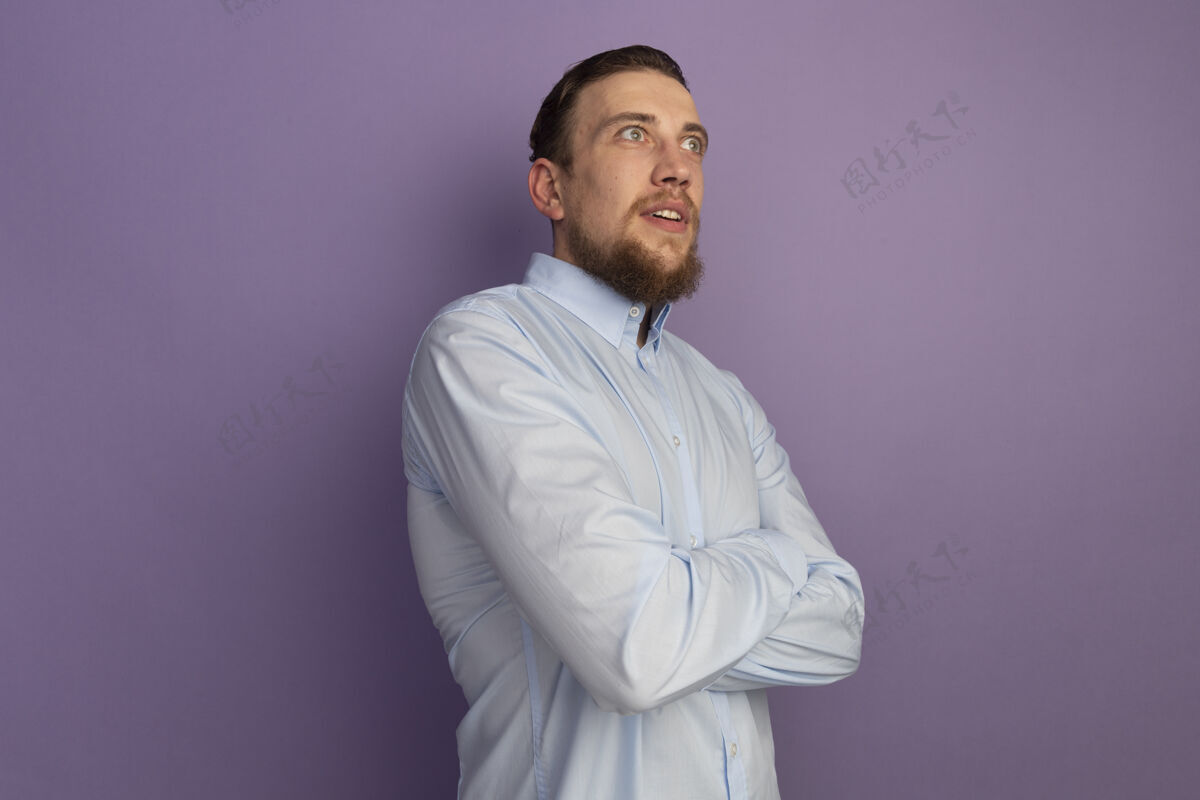 人兴奋的金发帅哥交叉双臂站在紫色的墙上 看着孤立的一面兴奋人表情