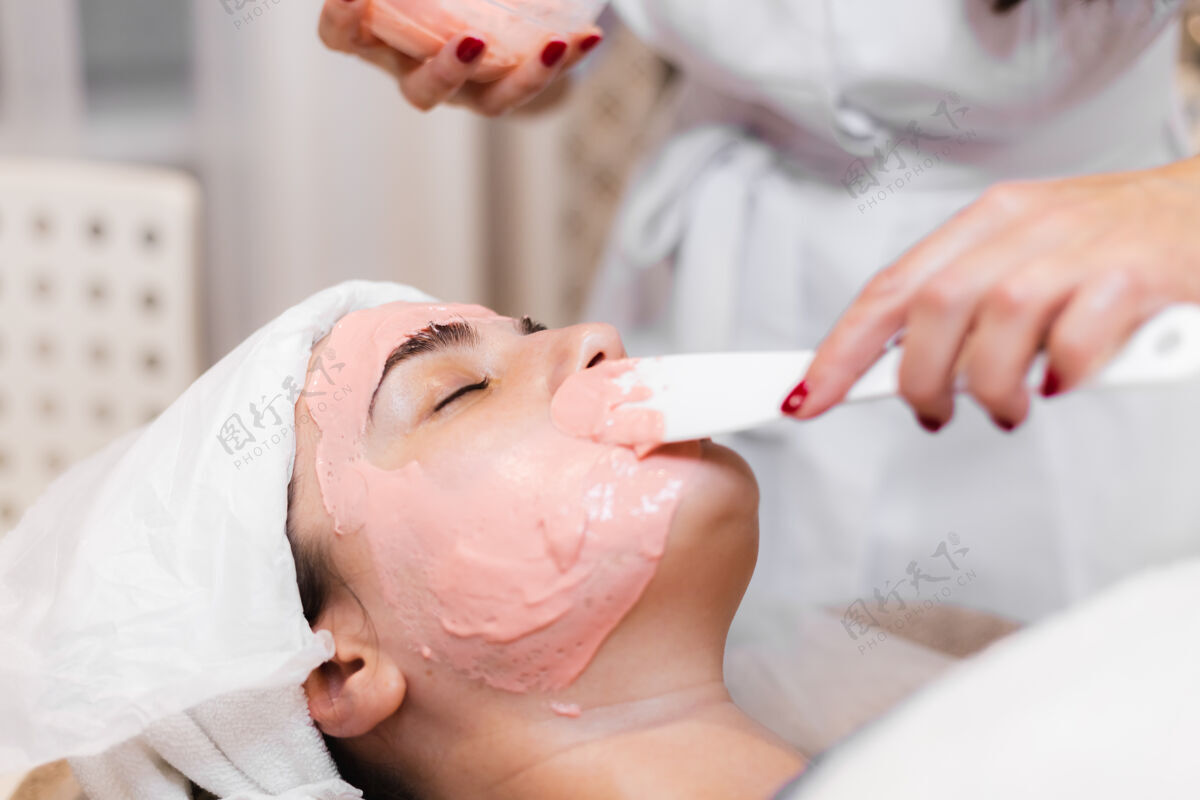 水疗美容师用抹刀在女人脸上敷海藻酸钠面膜治疗健康沙龙
