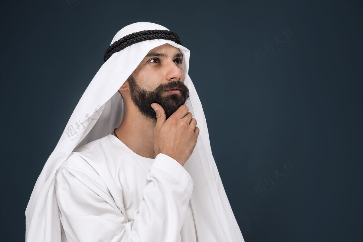 发呆深蓝色工作室背景上的半身阿拉伯沙特商人肖像年轻的男模站着 看起来很体贴商业 金融 面部表情 人类情感的概念东方震惊东方