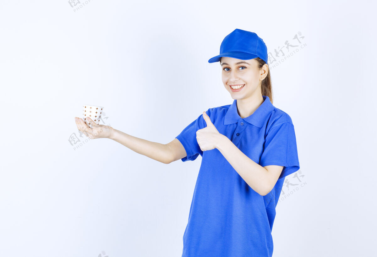 人穿着蓝色制服的女孩手里拿着一杯一次性饮料 并展示着享受的标志成人年轻人服装