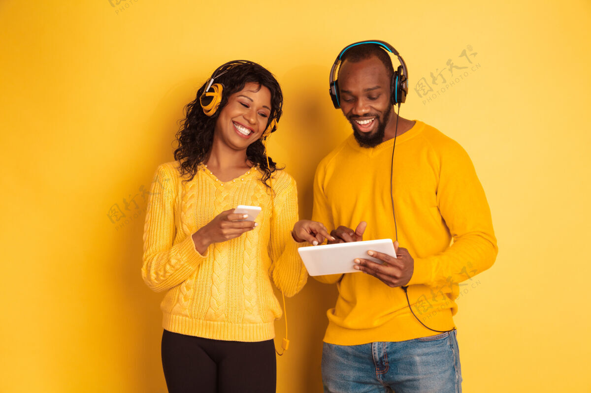 表情年轻感性的非裔美国人 穿着黄色背景的明亮休闲服美丽的情侣人类情感的概念 面部表情 关系 广告使用平板电脑和智能手机美国年轻成人