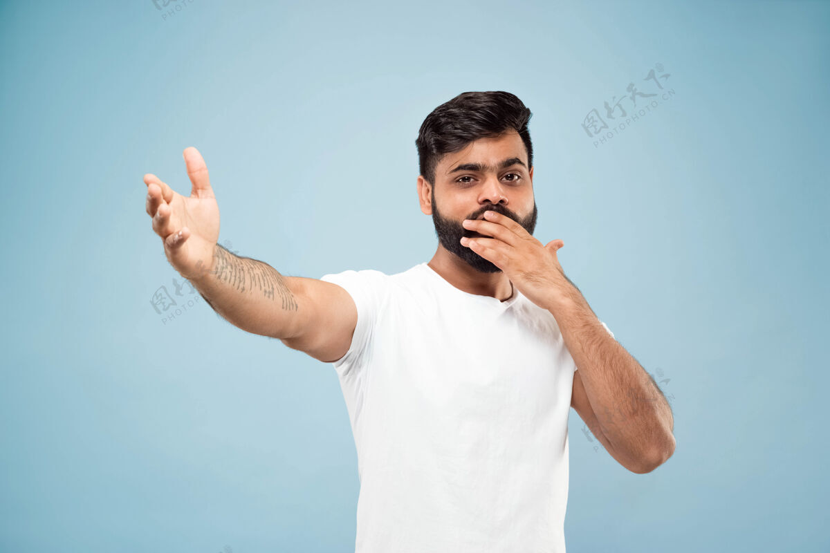 高管蓝色背景上穿着白衬衫的印度教年轻人的半身特写肖像人类情感 面部表情 销售 广告概念负面空间向上指快乐和惊讶面部工作惊讶
