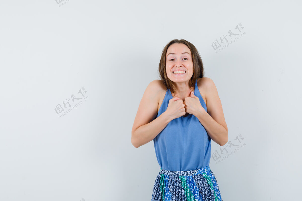 拳头年轻的女士在她的胸前握着拳头 微笑着穿着蓝色衬衫 裙子 看起来很高兴前视图文本空间诱惑头发肖像
