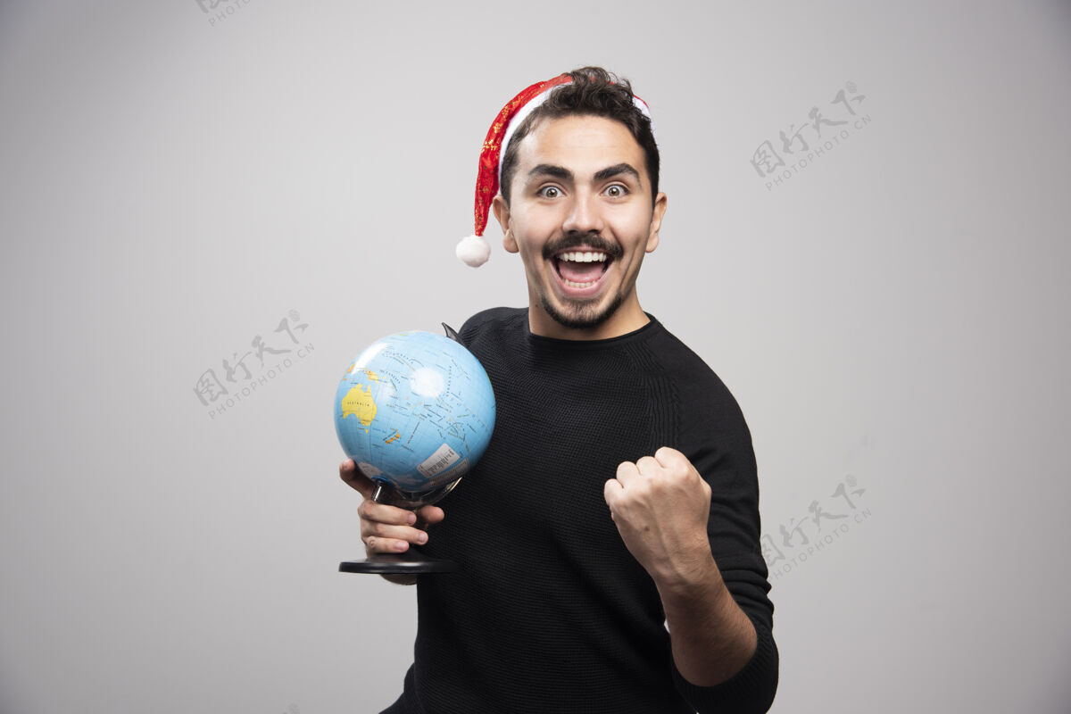 年轻戴着圣诞老人帽子拿着地球仪的快乐男人介绍时尚英俊