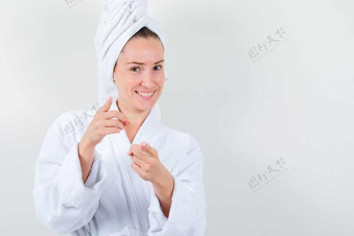 皮肤身着白色浴袍的年轻女士 用毛巾指着镜头 神情愉悦 前视图完美黑发干净