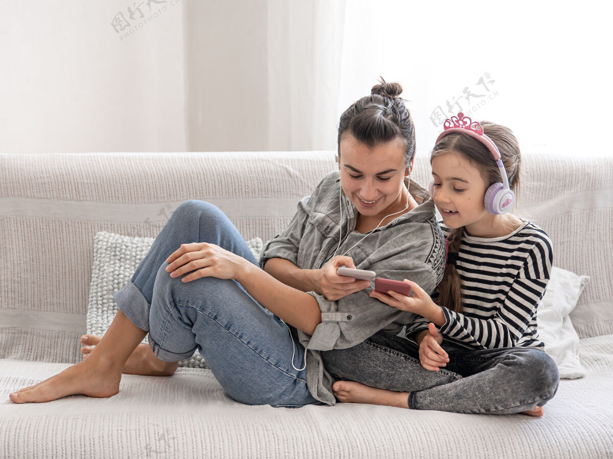 房子开朗的母女俩正在家里休息 戴着耳机听音乐这是一个幸福家庭和友好关系的概念孩子放松休闲