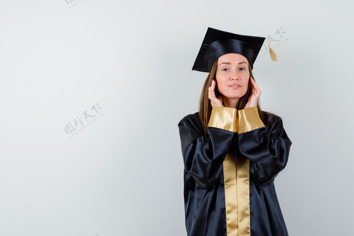 水疗年轻的女毕业生穿着学院服 手拉着脸颊 看上去自信满满 眼前一亮时尚女孩脸颊