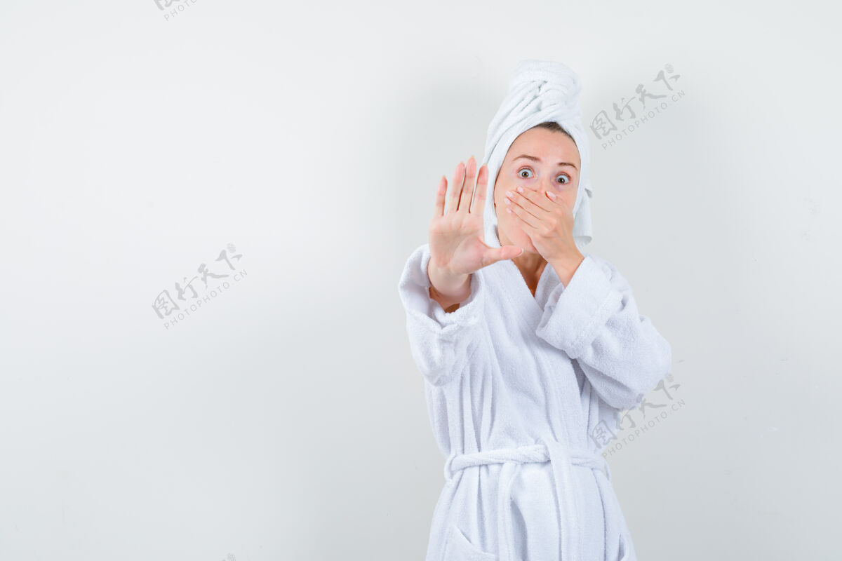 手势照片中的年轻女子手捂着嘴 穿着白色浴衣 毛巾做着停车的手势 看上去很害怕乐趣浴袍肖像