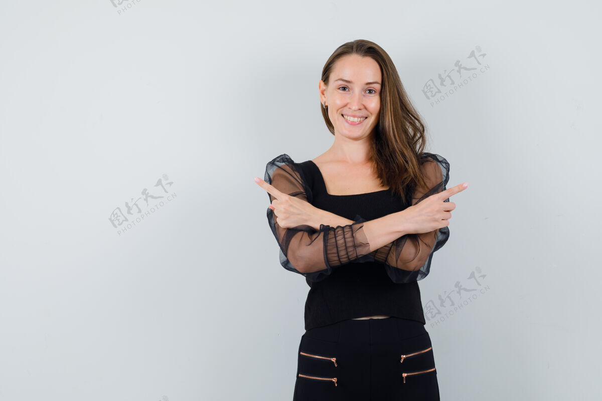 快乐一位年轻女子 双手穿着黑色上衣和黑色裤子 向相反的方向展示 看上去很开心正面图黑发头发衬衫