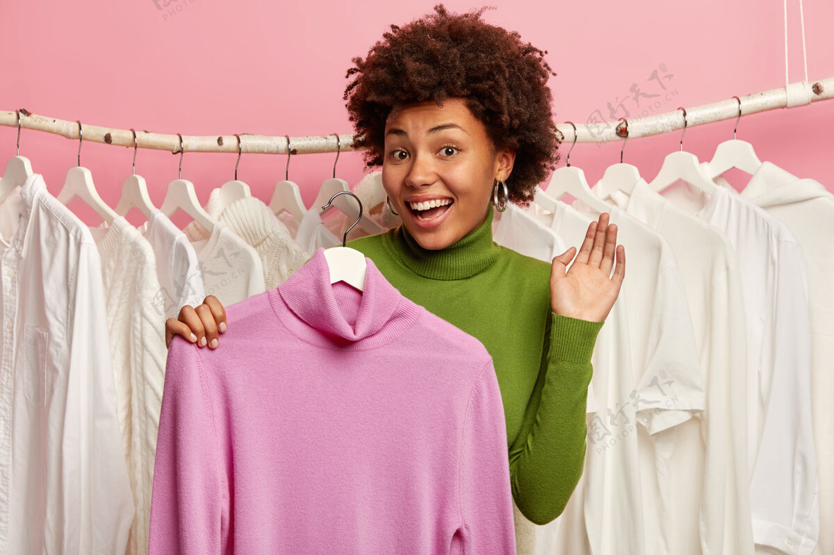 深色喜得黑皮肤的女人挑选衣服穿 把紫色的套头衫放在衣架上 靠着衣柜站着服装请购物狂