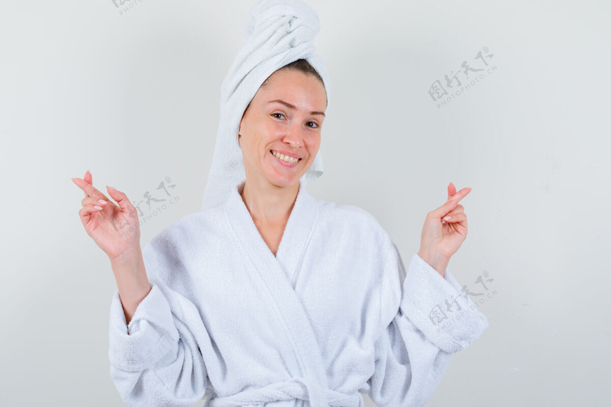 漂亮年轻的女士在白色浴衣 毛巾和手指交叉 看起来很高兴前视图头部前面护理