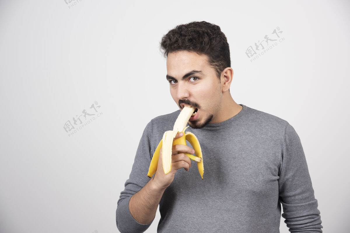 男孩一个年轻人在白墙上吃香蕉人时尚手