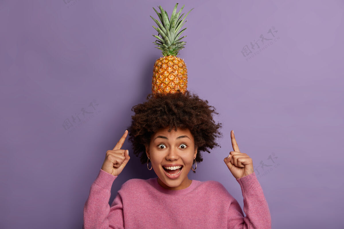 水果休息和寒冷看我怎么能高兴的卷发族女孩指着头上成熟的菠萝 积极地笑情感异国情调高兴