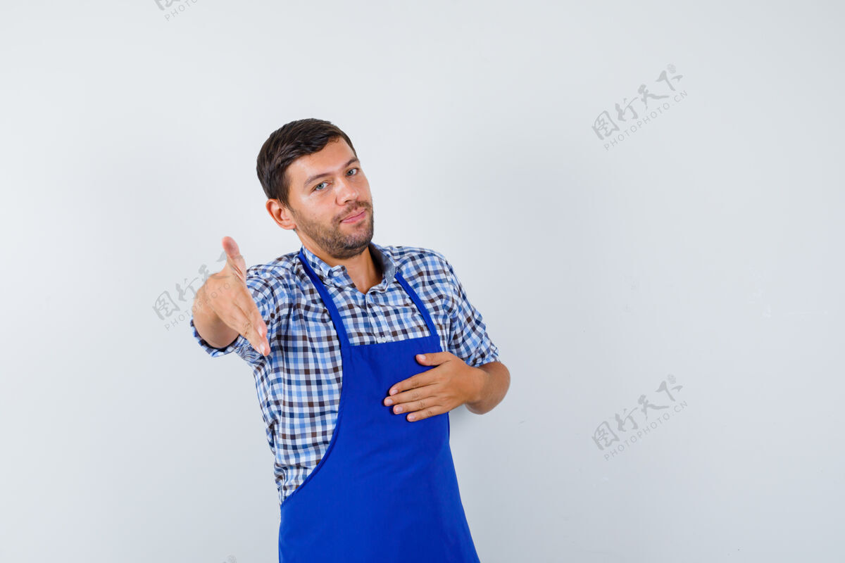 烹饪穿着蓝色围裙和衬衫的年轻男厨师男士衬衫厨师