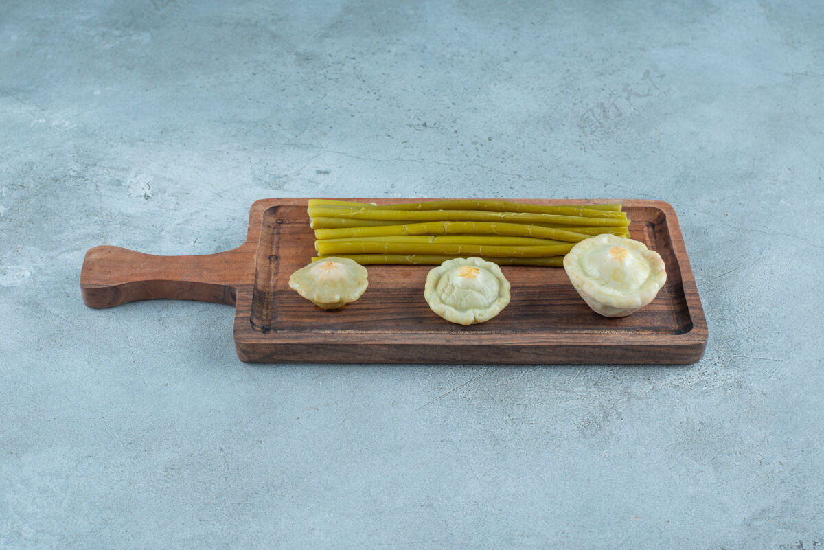 发酵美味的腌制小南瓜和棍子放在大理石表面的木板上棒子美味泡菜