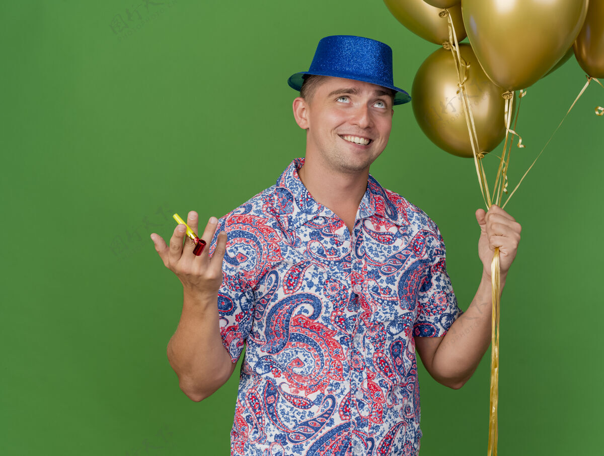 气球高兴的年轻人戴着蓝色的帽子 拿着气球与党吹隔离在绿色的背景拿着戴上小伙子
