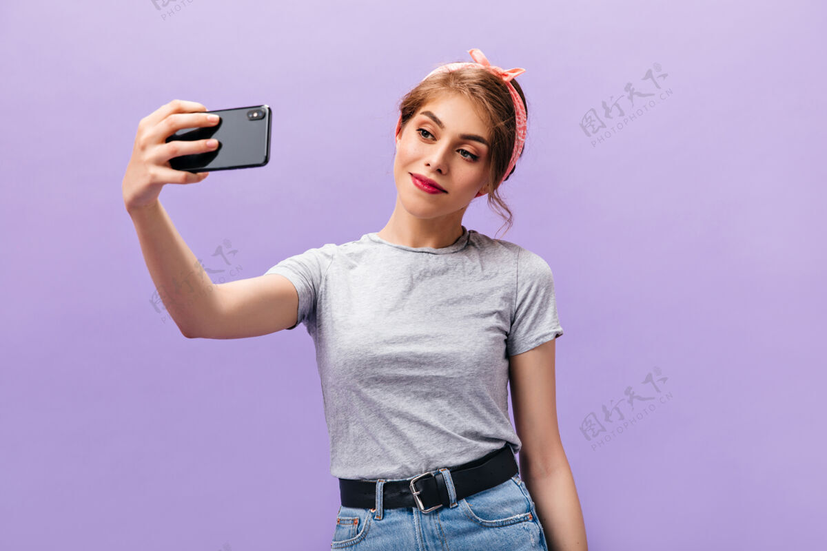 复制穿着灰色衬衫的女孩微笑着在紫色背景上自拍可爱的时髦女人 戴着粉色头带 穿着清凉的衣服拍照肖像头发姿势