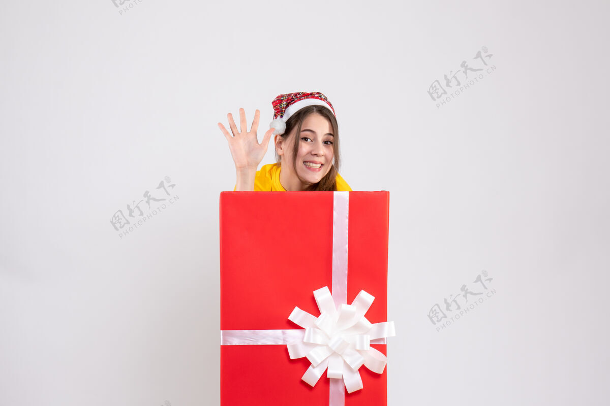 谚语前视图戴圣诞帽的可爱女孩在圣诞礼物后面打招呼节日笔记本圣诞老人