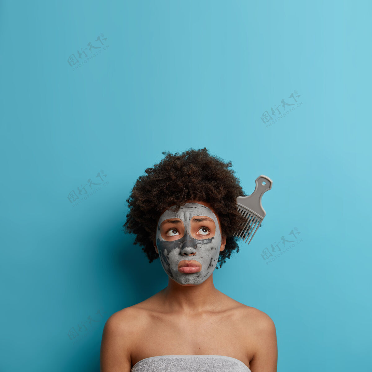 梳子失望压力大的女人有问题的卷发 卡住梳子 表达不满 涂泥面膜 关心身体和肤色 裹在毛巾里 隔离在蓝色的墙上 复制空间成人干燥凌乱