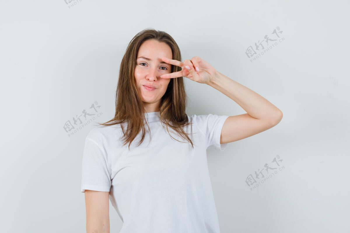 Vsign穿着白色t恤的年轻女士在眼睛附近显示v型标志 看起来很自信休闲黑发近