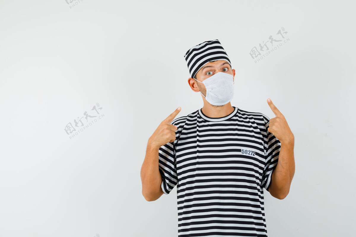 男性戴条纹t恤帽的年轻人指着他的医疗面罩休闲朋友T恤