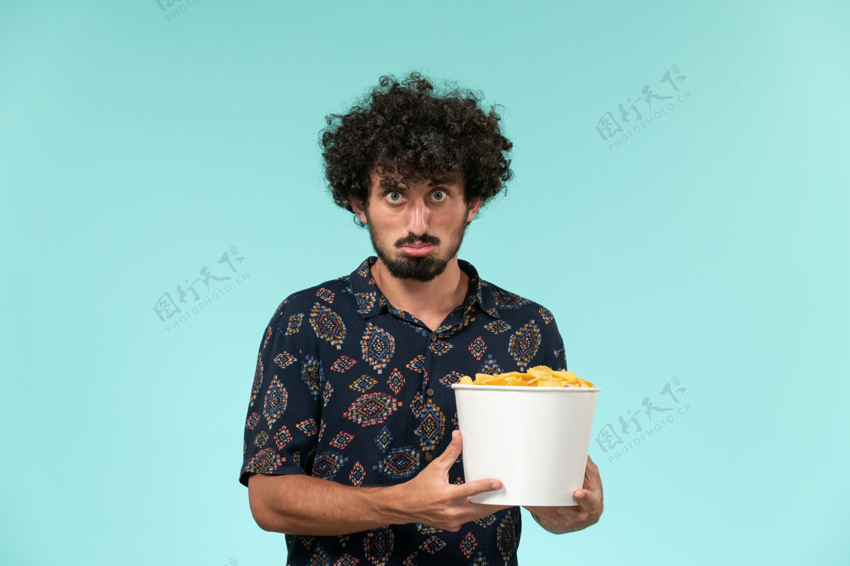 电影院前视图年轻人拿着篮子和土豆cips在蓝色的墙上看电影远程电影院电影炊具马克杯