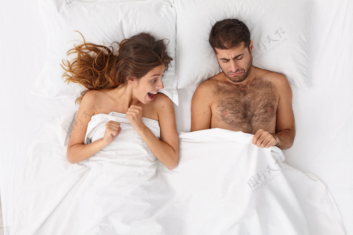 躯干好奇兴奋的女人一起躺在床上看着男人的生殖器不高兴的男人看着白色毯子下的阴茎 患有性功能障碍性问题 婚姻 关系观念问题成人悲伤