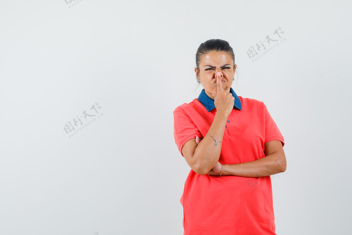 脸穿着红色t恤的年轻女子站在思考的姿势 把食指放在鼻子上 看起来很烦躁 正面视图女人鼻子化妆