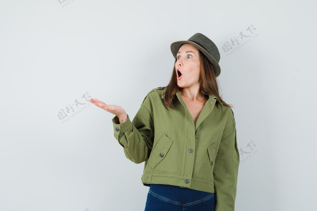 时尚年轻的女士摊开手掌在夹克裤子帽子 看起来很惊讶优雅裤子帽子