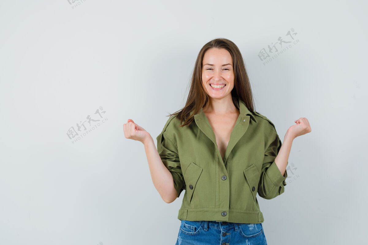 女性身着绿色夹克短裤的年轻女士展示着赢家的姿态 看上去很幸福短裤人类夹克