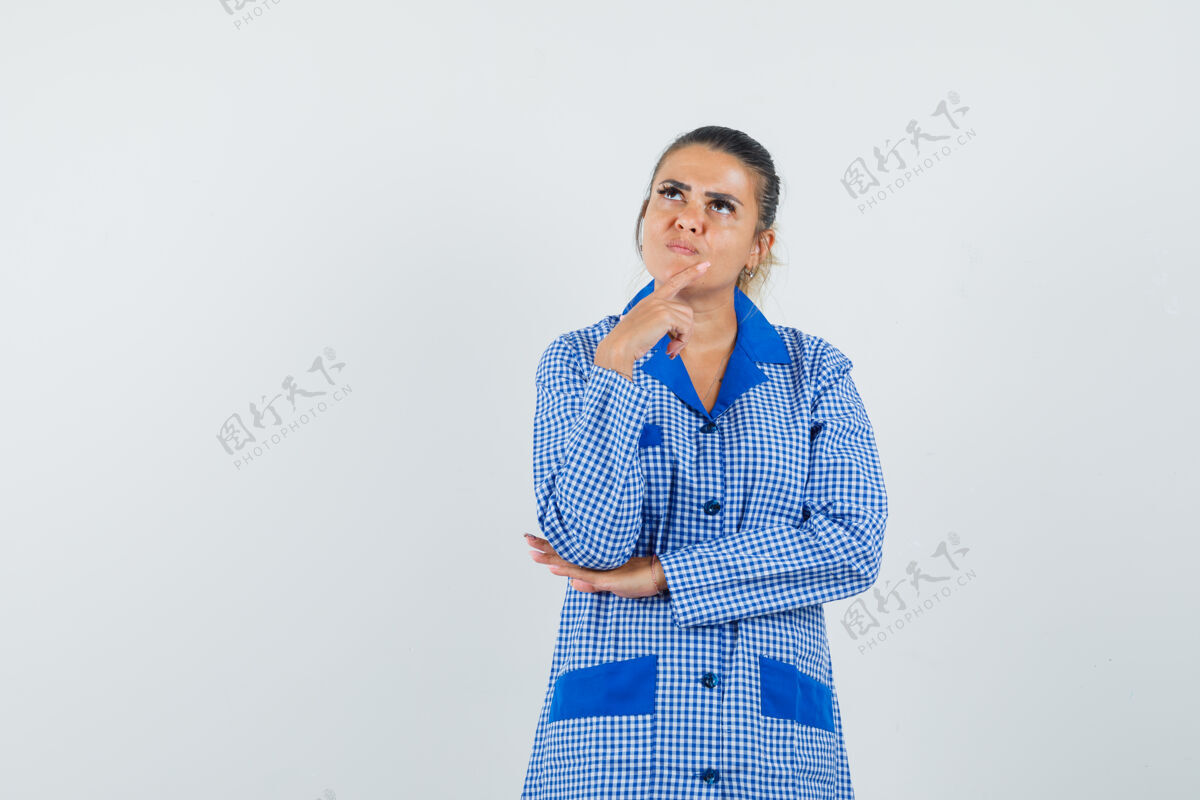 时尚年轻女子把食指放在下巴上 穿着蓝色方格布睡衣 站在那里思考 神情沉思前视图成人方格布女性