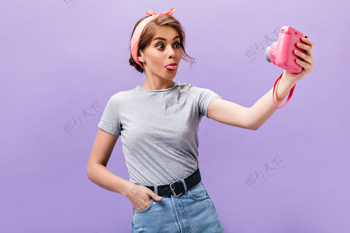 牛仔裙意气风发的女人露出舌头 自拍穿着粉色大手帕和时髦服装摆姿势的有趣迷人的女人紫色背景肖像头发姿势