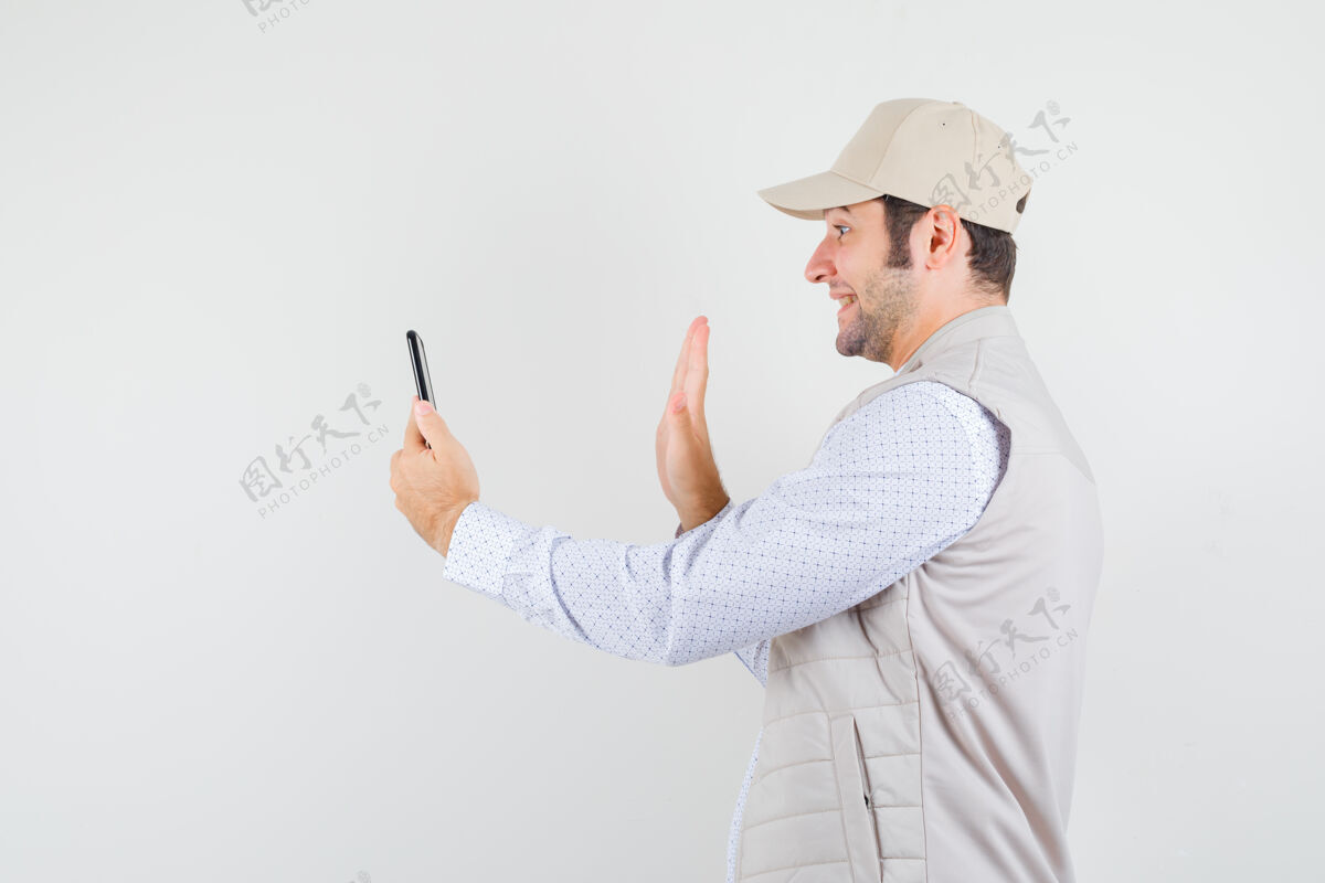 时尚一个年轻人拿着手机 戴着米色夹克和帽子通过视频通话 看上去很开心 正对着前方男性脸花花公子