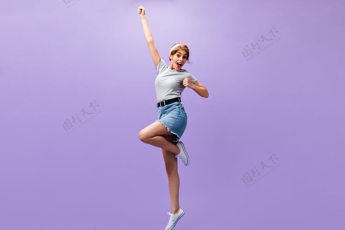 脸穿着裙子和衬衫的快乐女人跳到紫色背景上心情愉快的年轻女孩穿着时髦的服装摆姿势孤立的背景时尚紫色衬衫