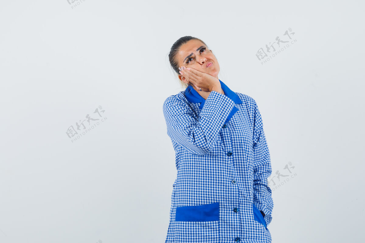 亚洲年轻女子面颊靠在掌心 站在思考的姿态在蓝色格子睡衣衬衫和期待沉思 前视图女性脸干净
