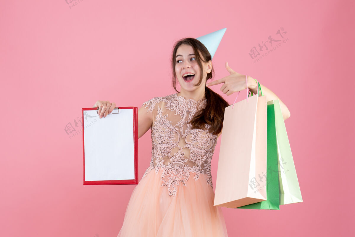 人前视图兴高采烈的女孩与党帽举行文件和购物袋指着自己公主指着购物