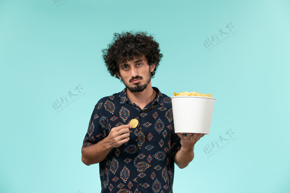 篮子正面图年轻人拿着篮子和土豆cips 在蓝色的墙上吃电影男电影土豆电影