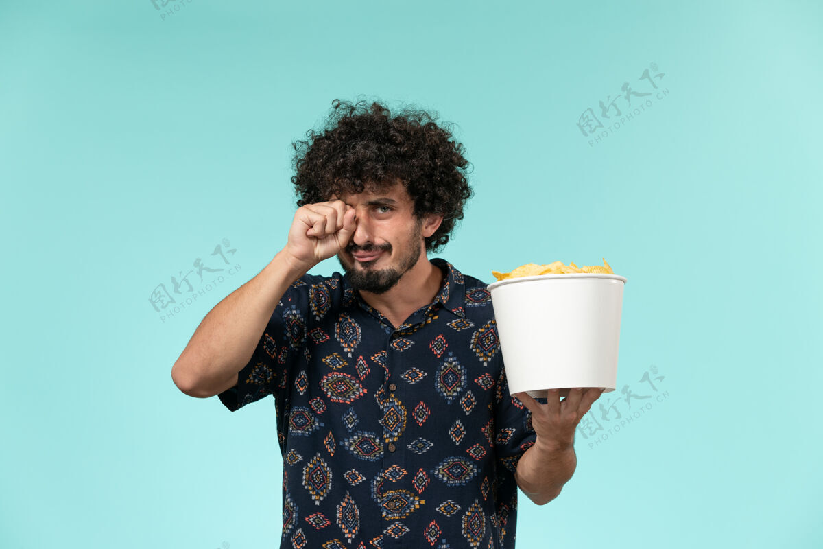 杯子正面图：年轻人拿着篮子 拿着土豆 在蓝墙电影院看电影哭男看年轻人视图