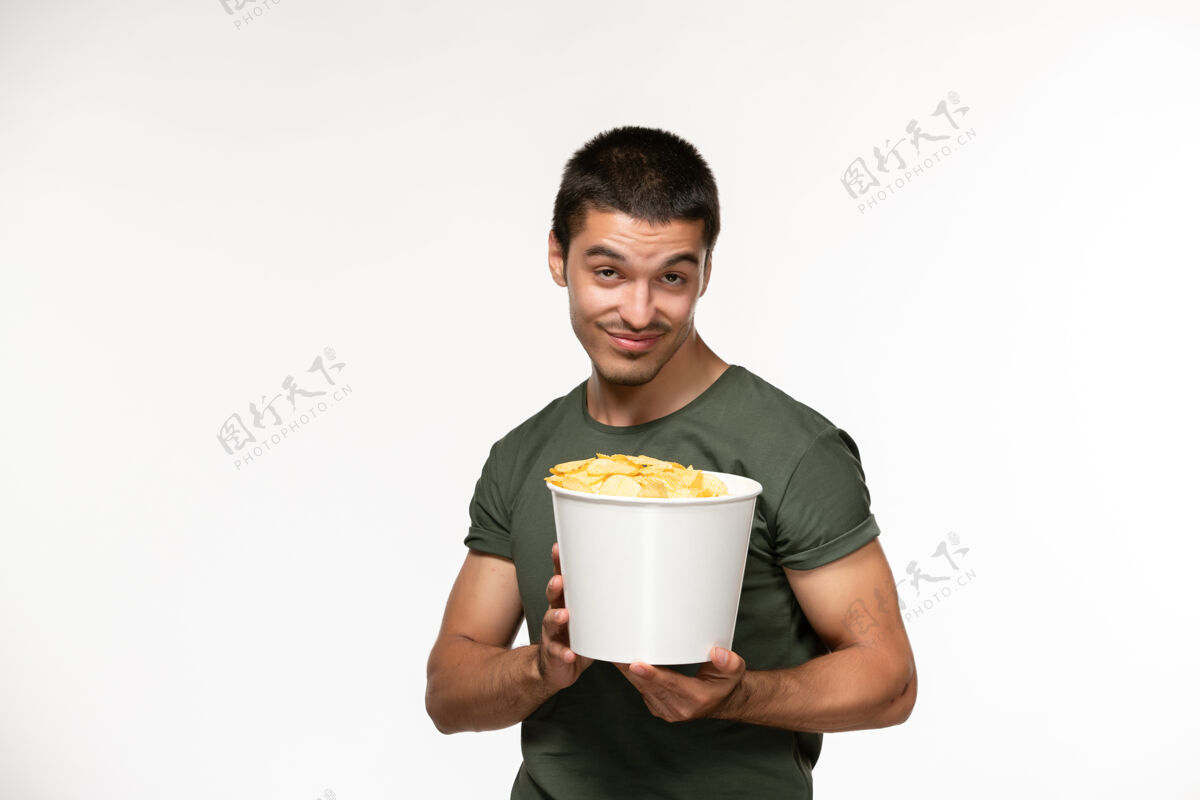 土豆正面图身穿绿色t恤的年轻男子拿着土豆cips放在白色书桌上孤独的人看电影卡布奇诺早餐视图