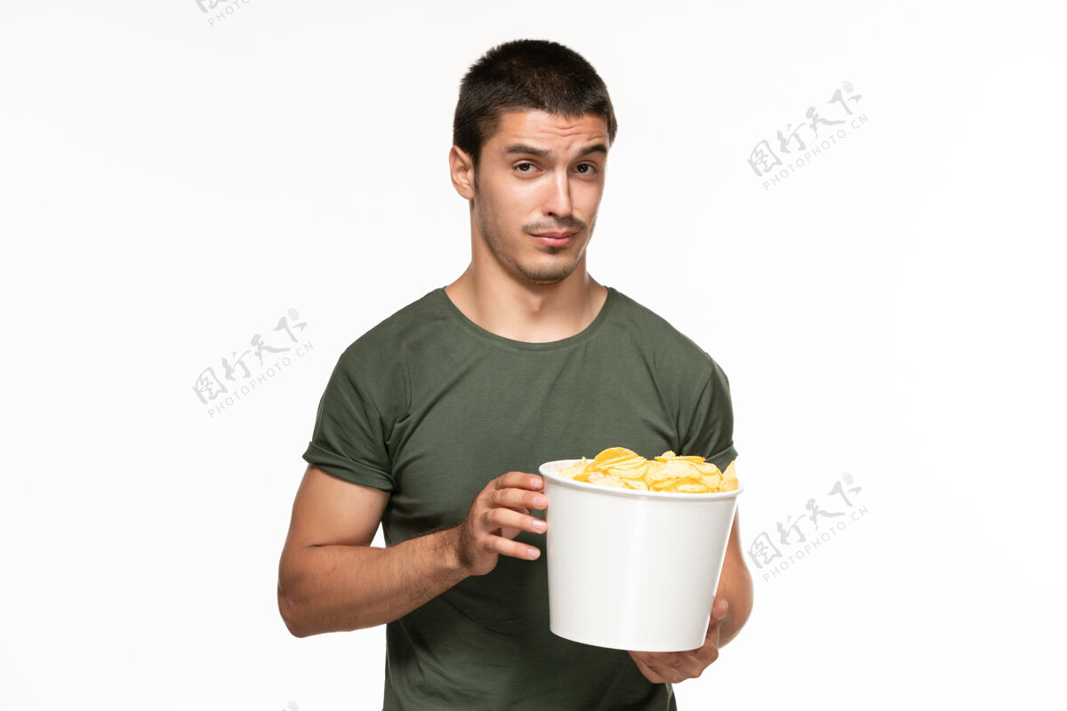 土豆正面图身着绿色t恤的年轻男子拿着篮子 在白色墙上放着土豆 孤独地享受着电影的乐趣电影享受篮子