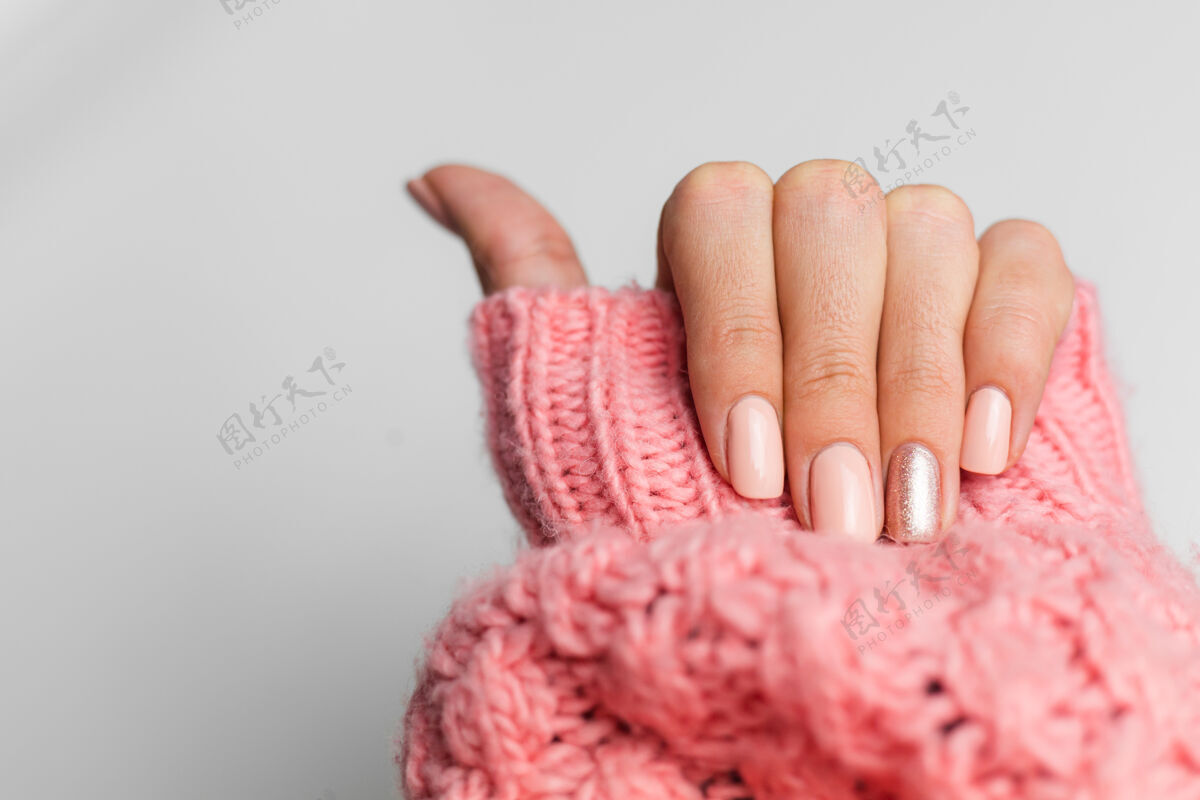 治疗漂亮的裸色美甲 一个手指闪亮的金色 在针织粉色羊毛枕头的背景下美容师明亮衣服