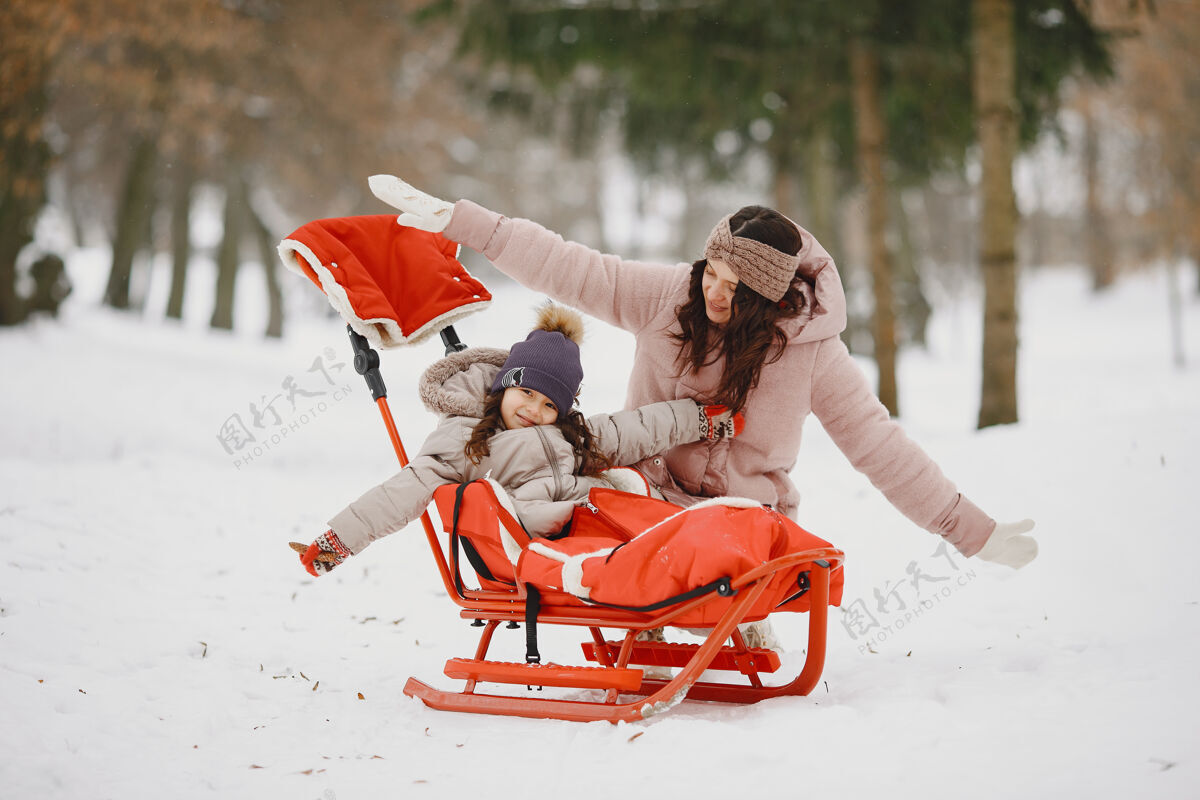 衣服带着雪橇的公园里的女人和小女孩父母女儿自然