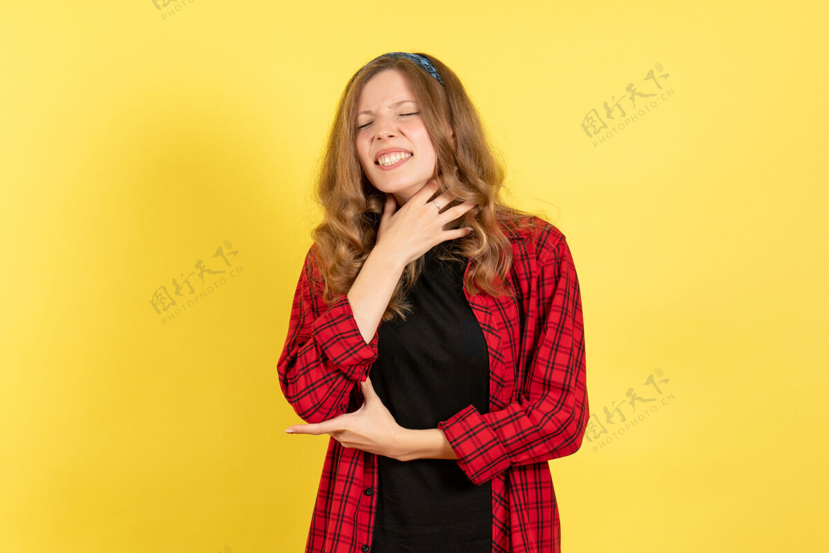 格子正面图身着红色格子衬衫的年轻女性在黄色背景上摆姿势女孩女性情感模特彩色人类前面女孩观点