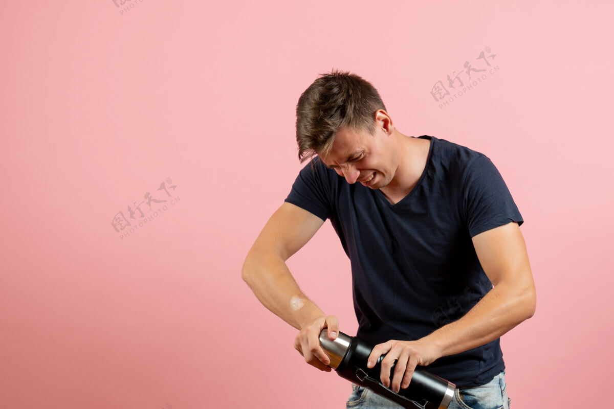 人正面图：身穿深蓝色衬衫的年轻男性手持热水瓶 试图打开粉色背景上的人类男性情感模型颜色骑自行车尝试观点