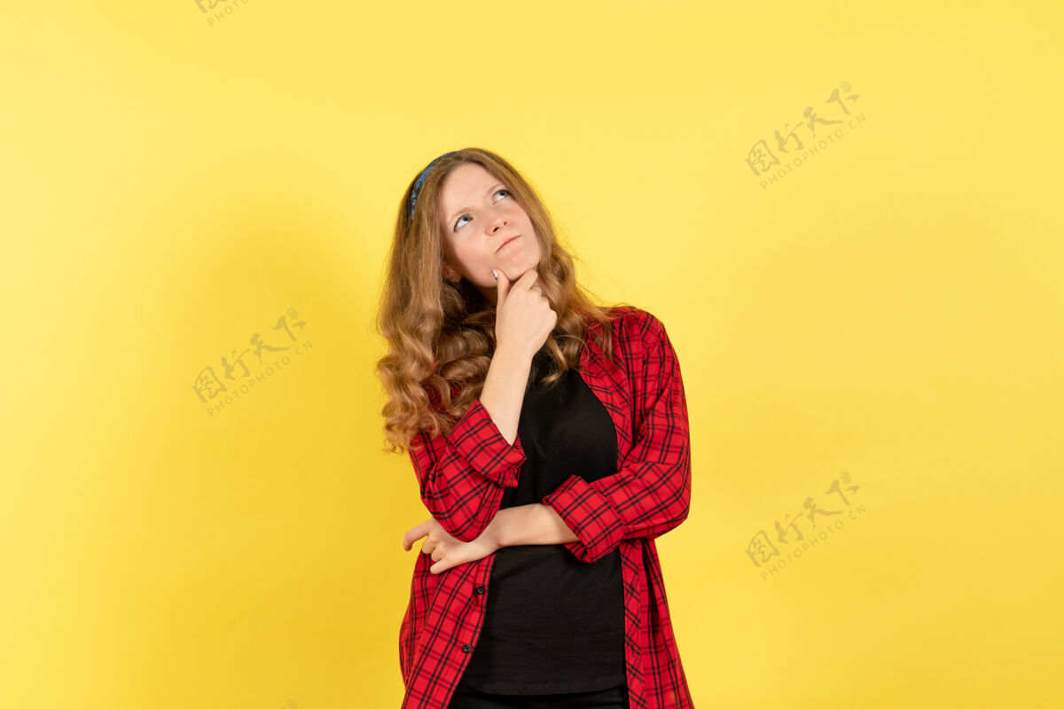 思考正面图穿红色格子衬衫的年轻女性在黄色背景上摆姿势思考女人人类情感模特时尚女孩肖像年轻女性前面