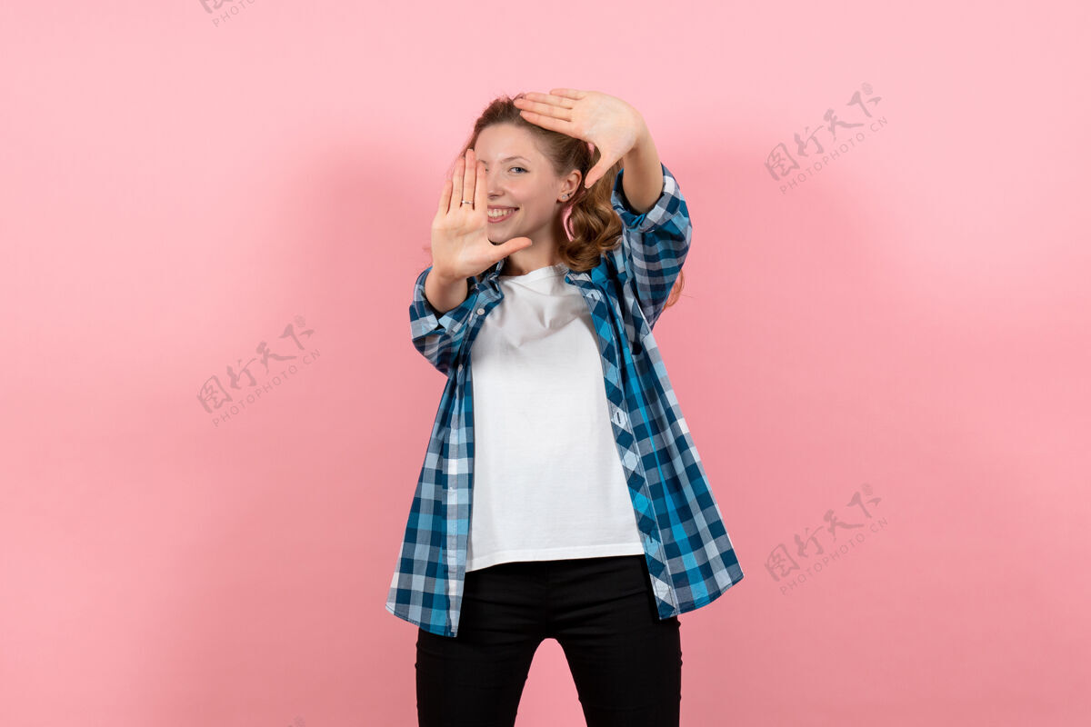 微笑正面图身着蓝色格子衬衫的年轻女性在粉色背景上微笑摆姿势童女青春情感模特时尚女孩格子电话