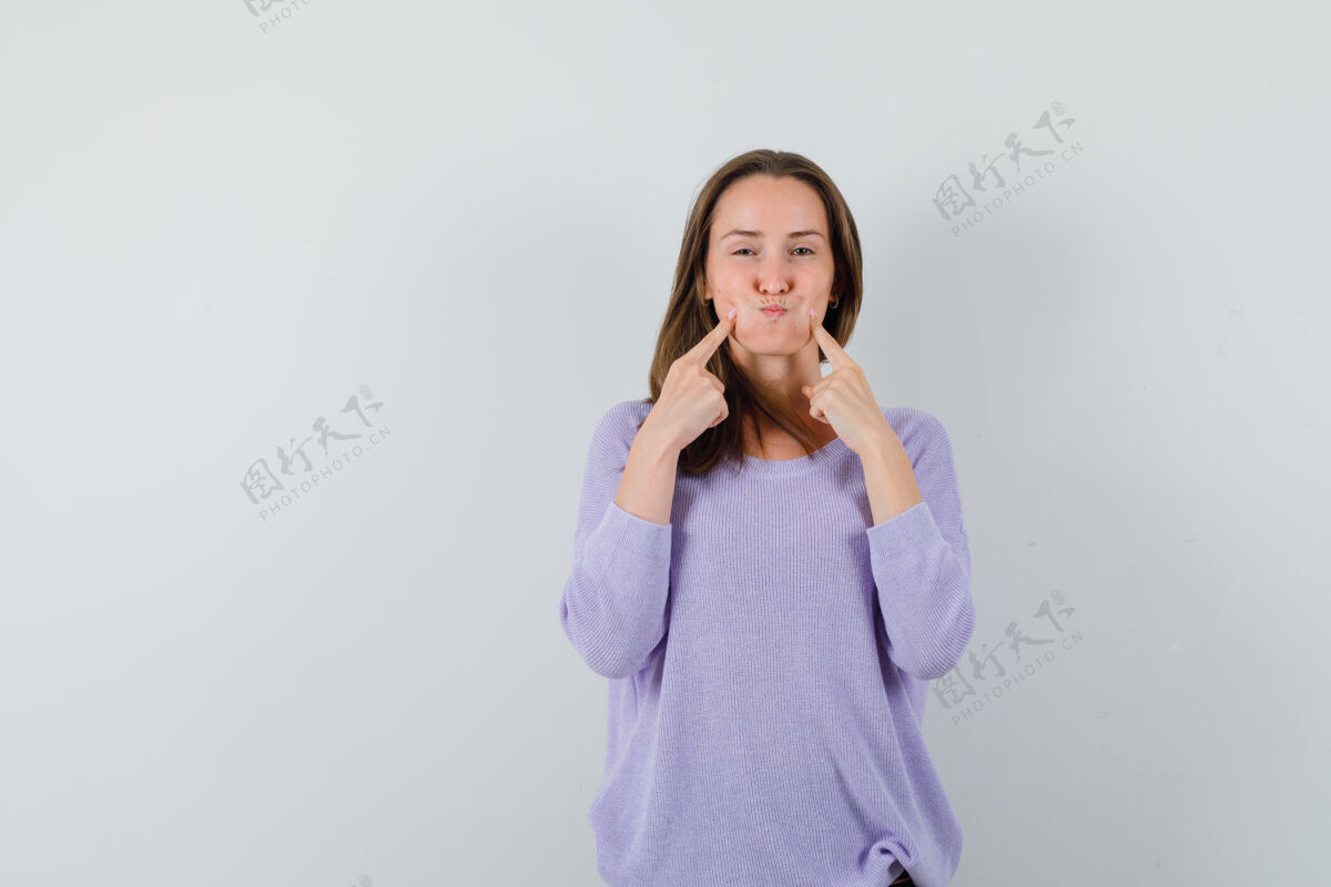 漂亮穿着休闲衬衫的年轻女士用手指抚摸着吹皱的脸颊 看上去很有趣正面图魅力女士护理