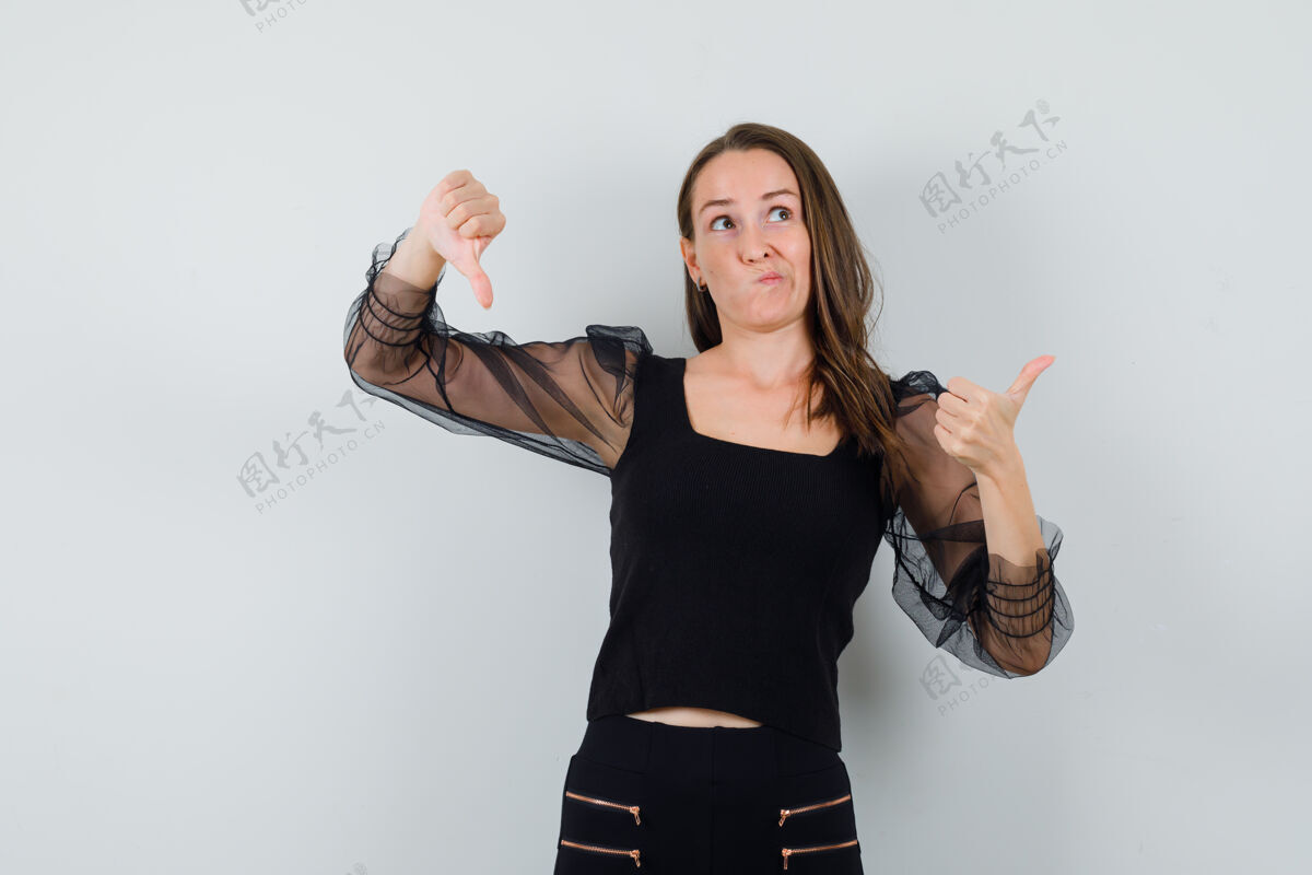 向上一个穿黑衬衫的年轻女人上下竖起大拇指 看上去很困惑卷曲手姿势