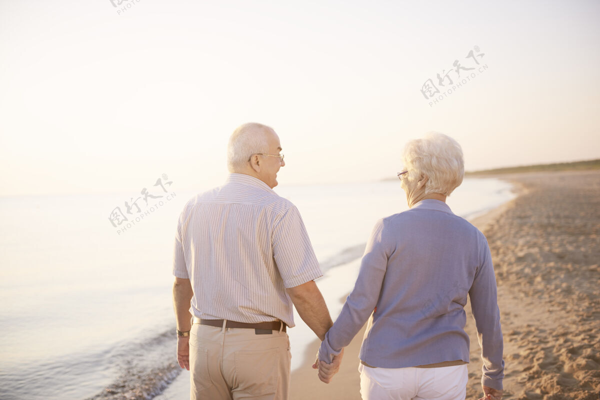 祖母手牵着手走在沙滩上退休散步海洋